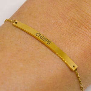 Könnte beinhalten: Goldkette Armband mit einem goldenen Barren Anhänger, der mit dem Wort "CHIEFS" graviert ist.