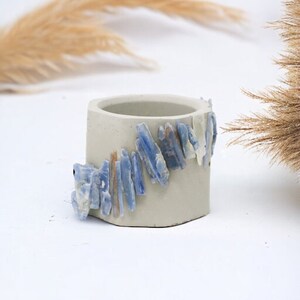 May include: A small, gray concrete planter with a decorative band of blue and white crystal shards.