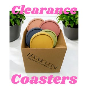 May include: A set of six colorful coasters in a cardboard box. The coasters are round and made of a smooth material. The box is brown and has the text "LEX MODERNE MODERN BOHEMIAN ART" printed on it.
