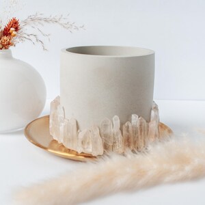 Puede incluir: Una maceta de hormigón blanco con un borde dorado y un borde de cristales de cuarzo transparentes.