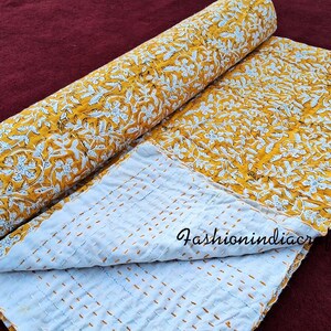 Puede incluir: Una colcha kantha amarilla y blanca con un patr&oacute;n floral. La colcha est&aacute; doblada por la mitad y tiene un respaldo blanco con costuras amarillas.