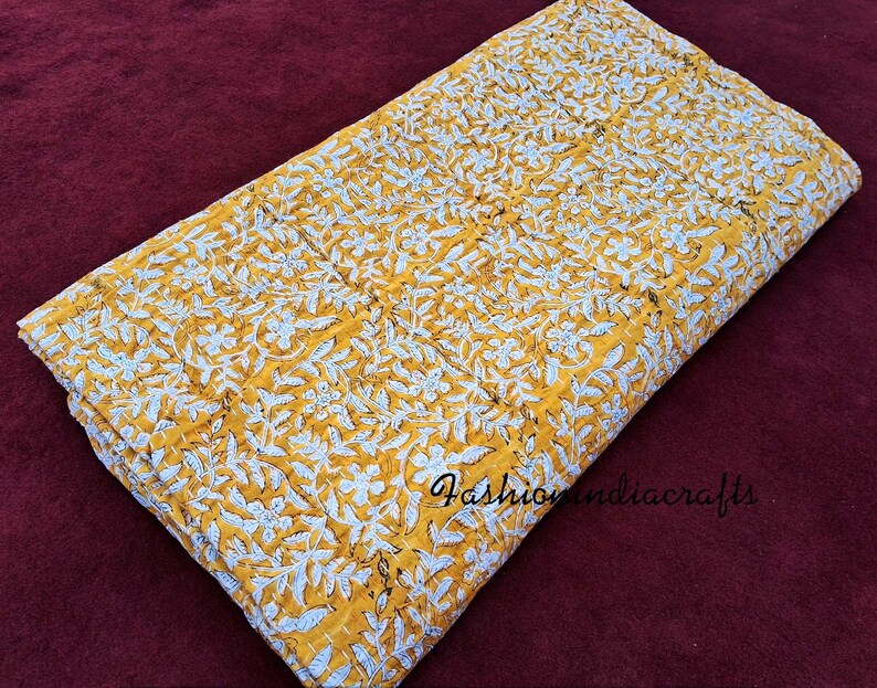 Puede incluir: Una colcha kantha amarilla y blanca con un patr&oacute;n floral. La colcha est&aacute; hecha de algod&oacute;n y est&aacute; cosida a mano. Es un textil indio tradicional.