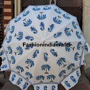 May include: White parasol featuring a blue floral design and the text "fashionindiacrafts". The umbrella has a scalloped edge with a blue and white striped border. The design includes stylized palm trees and other floral elements.