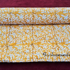 Puede incluir: Una colcha kantha amarilla y blanca con un patr&oacute;n floral. La colcha est&aacute; doblada por la mitad y tiene una etiqueta blanca con el texto "fashionindiacrafts".