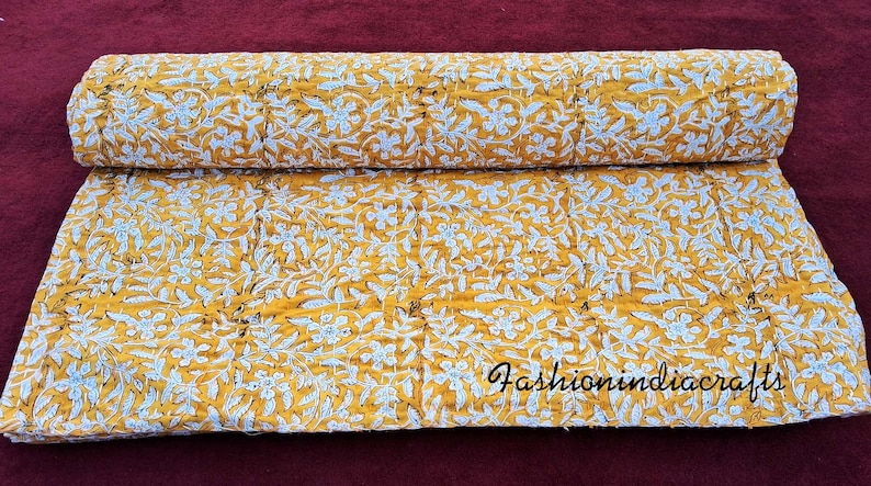 Puede incluir: Una colcha kantha amarilla y blanca con un patr&oacute;n floral. La colcha est&aacute; doblada por la mitad y tiene una etiqueta blanca con el texto "fashionindiacrafts".