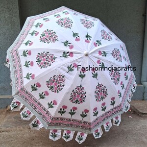 Può includere: Un ombrellone bianco con un motivo floreale ripetuto stampato in rosa e verde. Il bordo della copertura è decorato con una bordura geometrica rosa e verde e piccole linguette di tessuto. Il testo Fashionindiacrafts è visibile.