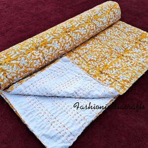 Puede incluir: Una colcha kantha floral amarilla y blanca con un respaldo blanco. La colcha est&aacute; doblada por la mitad y est&aacute; sobre una superficie marr&oacute;n.