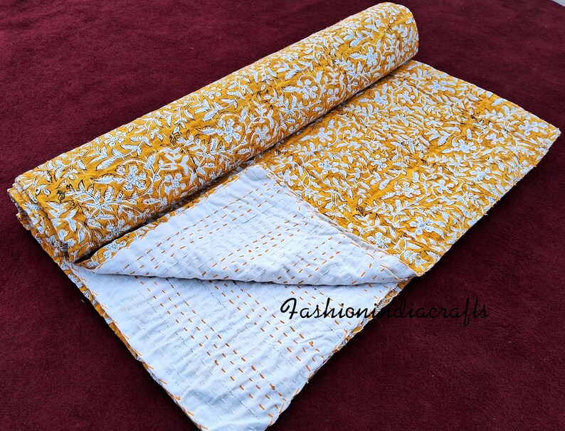 Puede incluir: Una colcha kantha floral amarilla y blanca con un respaldo blanco. La colcha est&aacute; doblada por la mitad y est&aacute; sobre una superficie marr&oacute;n.
