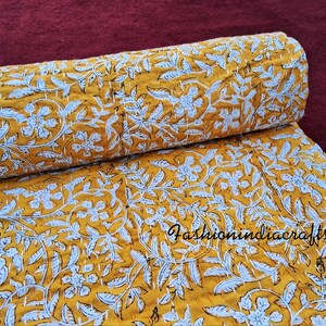 Puede incluir: Una colcha kantha amarilla con un patr&oacute;n floral blanco. La colcha est&aacute; doblada por la mitad y la tela es texturizada.