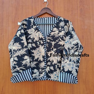 May include: A quilted jacket featuring a black base with a beige floral pattern, a V-neckline, and long sleeves with folded cuffs. The interior and cuffs display a black and white vertical striped pattern. The text Fashionindiacrafts is visible.