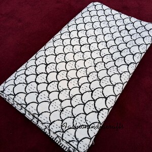 May include: White cotton fabric with a black and white geometric pattern of overlapping circles. The fabric is folded and has a slight sheen.