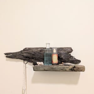 May include: A rustic wooden shelf made from driftwood with a small shelf and a hook. The shelf is decorated with two bottles of body spray, a seashell, a necklace, and a bracelet with the word "Faith" on it.