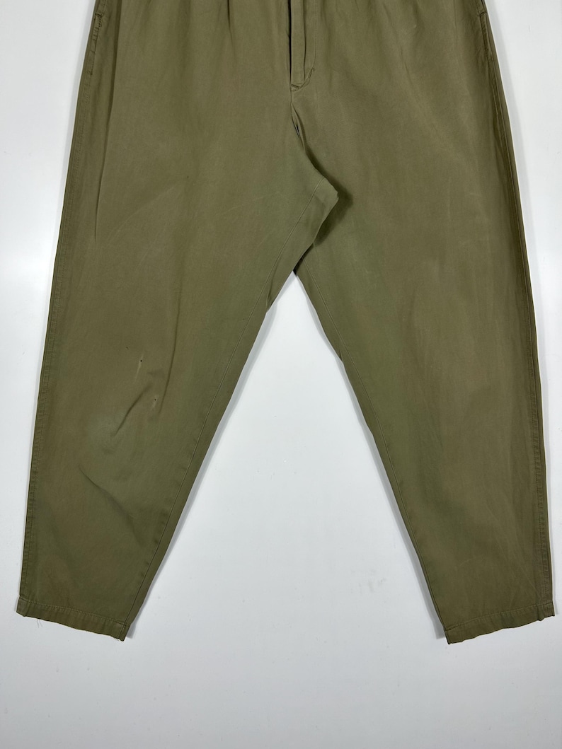 Puede incluir: Pantalones verde oliva con cintura el&aacute;stica y cierre de bot&oacute;n. Los pantalones tienen un corte relajado y un aspecto ligeramente descolorido. La tela parece ser una mezcla de algod&oacute;n duradera.