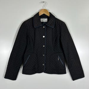 May include: Black quilted jacket with a diamond pattern, featuring a collar and button closure. The jacket has two front pockets with zippers and navy blue trim. The brand name "courr&egrave;ges" is visible on the label.
