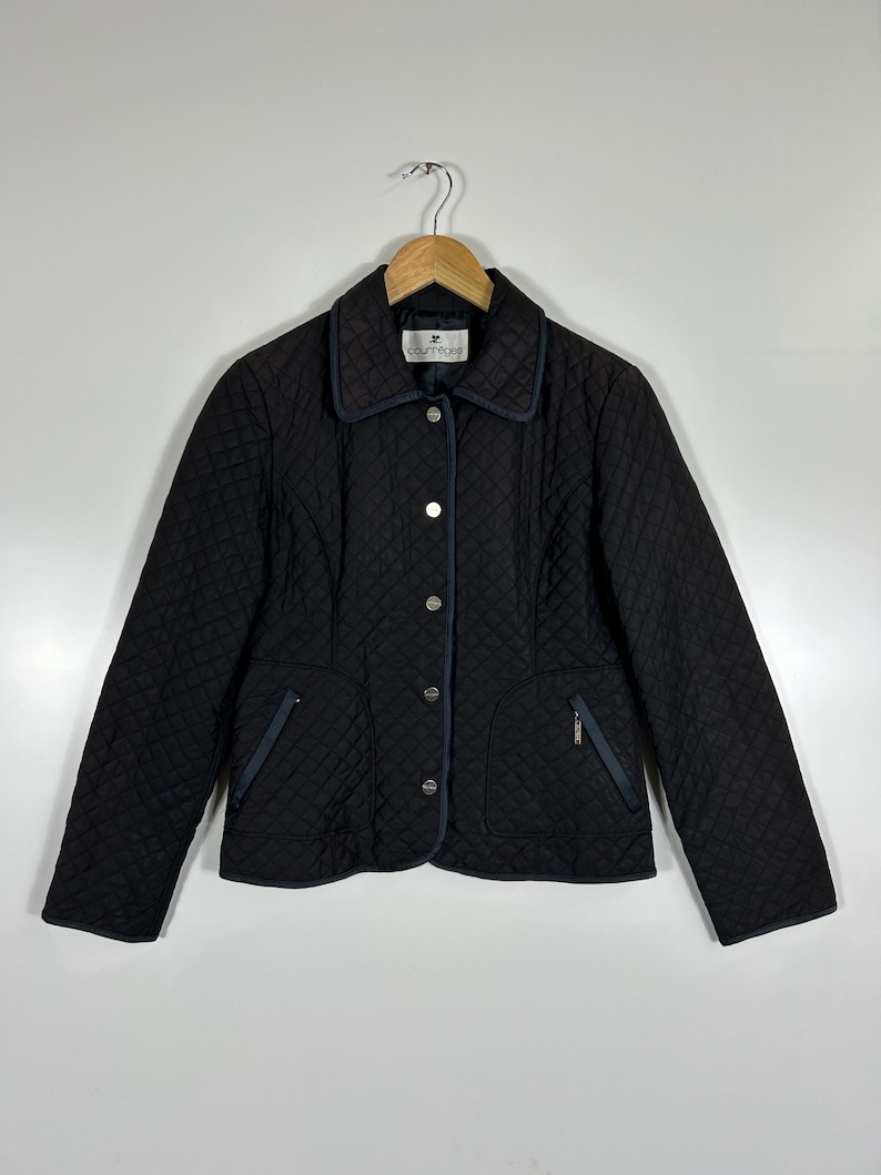 May include: Black quilted jacket with a diamond pattern, featuring a collar and button closure. The jacket has two front pockets with zippers and navy blue trim. The brand name "courr&egrave;ges" is visible on the label.