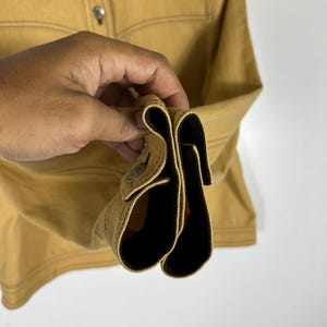 Peut inclure: Une chemise &agrave; manches longues jaune moutarde dot&eacute;e d'un col pointu, d'une patte de boutonnage avant avec des boutons m&eacute;talliques et de boutons m&eacute;talliques assortis aux poignets. Le v&ecirc;tement pr&eacute;sente des surpiq&ucirc;res visibles le long des coutures.