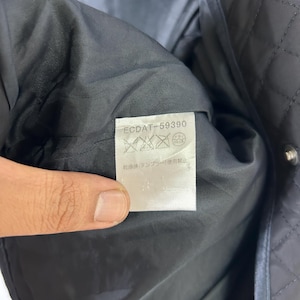May include: Close-up of a black quilted jacket interior. The inside lining is black and smooth. A white tag with the text "ECDAT-59390" and care symbols is visible. The jacket has silver snap closures.