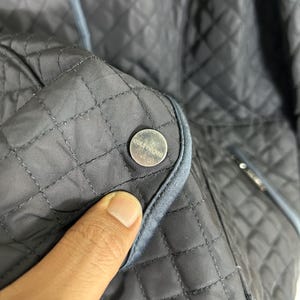 May include: Close-up of a dark gray quilted jacket with a silver button. The jacket has a diamond pattern and light blue trim. The button has the word "couture" on it.