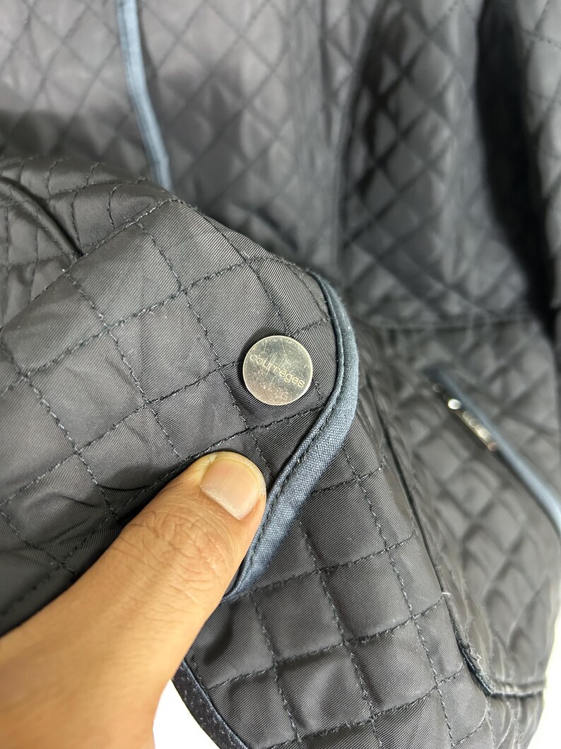 May include: Close-up of a dark gray quilted jacket with a silver button. The jacket has a diamond pattern and light blue trim. The button has the word "couture" on it.