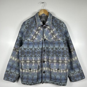 Può includere: Giacca fantasia blu, grigia e bianca, con due tasche frontali e chiusura con bottoni. La giacca ha un colletto e maniche lunghe. Il nome del marchio "VALE" è visibile sul colletto.