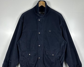 Puede incluir: Chaqueta azul marino con cuello alzado, dos bolsillos delanteros y botones plateados. La chaqueta tiene un diseño clásico y está hecha de un material suave. La chaqueta está colgada en una percha.