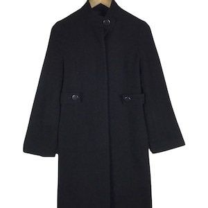 May include: A black wool coat with a stand-up collar and two button closures. The coat has two front pockets and long sleeves. It is hanging on a wooden hanger against a white background.