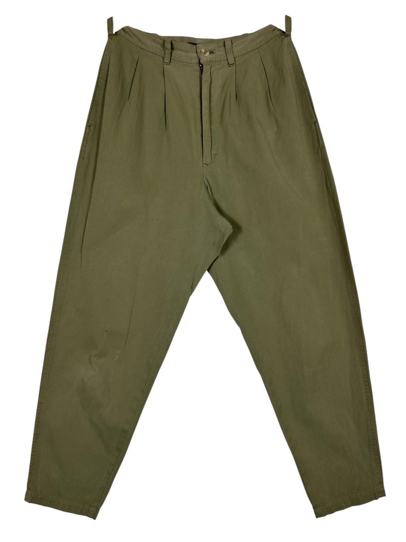 Puede incluir: Pantalones plisados ​​verde oliva con cierre de bot&oacute;n y cremallera. Los pantalones tienen un corte holgado y una cintura alta. La tela parece ser un algod&oacute;n ligero o una mezcla. Los pantalones son de color liso y tienen un estilo cl&aacute;sico y vintage.