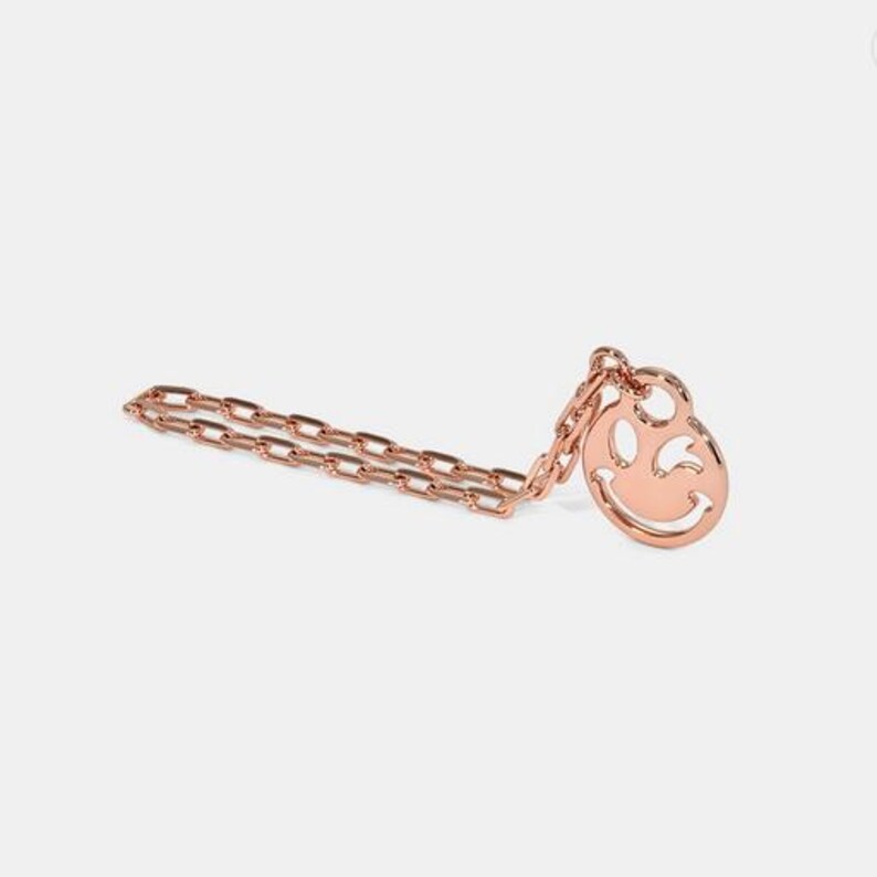 May include: A rose gold necklace with a smiley face pendant. The chain is a delicate, linked style.
