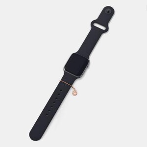 May include: A black silicone watch band with a silver watch face and a small gold charm attached to the band.