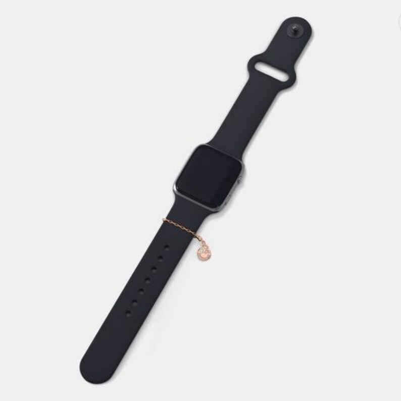 May include: A black silicone watch band with a silver watch face and a small gold charm attached to the band.