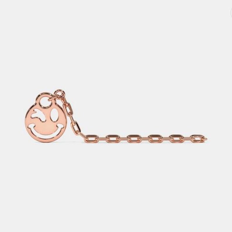 May include: A gold chain necklace with a winking smiley face charm.