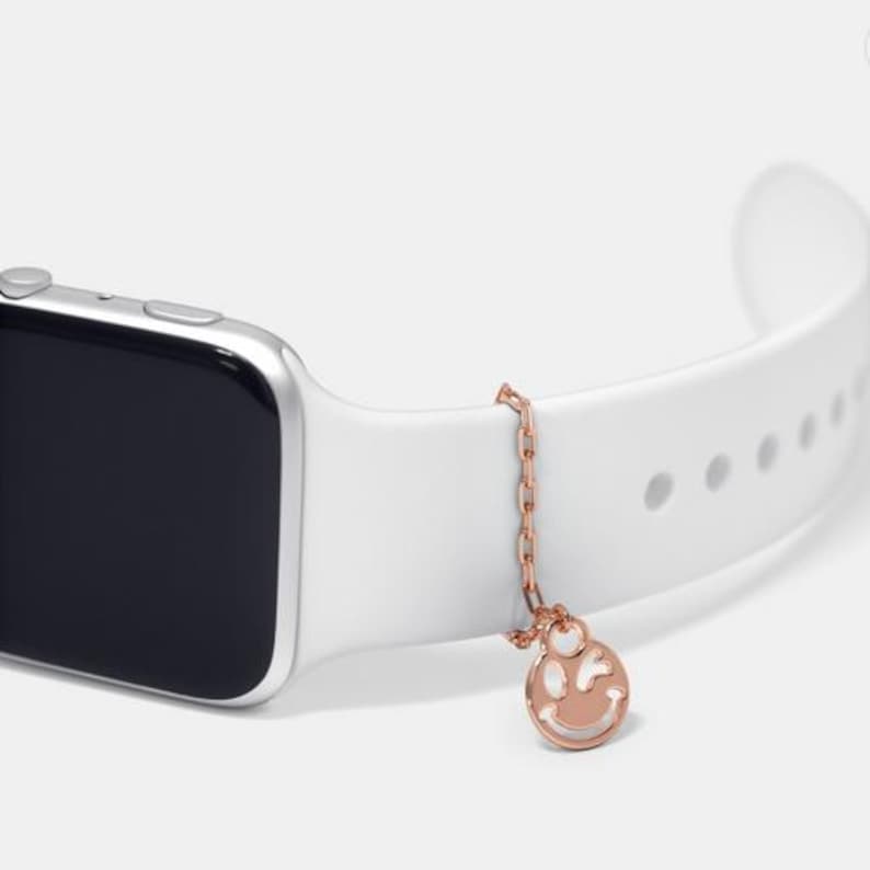 May include: A white Apple Watch band with a rose gold chain and a charm with a smiley face cutout.