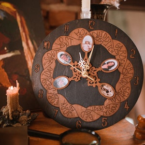 May include: A dark brown wooden clock with a unique design. The clock face features a circular band with the words "GARDEN", "QUIDDITCH", "LOST", "HOME", "WORK", "BED", "MORIAL", "PERIL", "SCHOOL", "SOUFTS", "HOLIDAY", "FOREST" written around the edge. The clock hands are gold, and there are small photo frames with pictures of people and a dog.