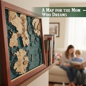 May include: A framed wooden map with a layered design, featuring a teal blue background and light brown landmasses. The map is in a dark brown frame and has the text "A Map for the Mom Who Dreams".