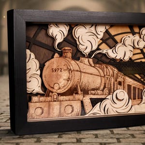 Puede incluir: Obra de arte en madera enmarcada que representa un tren de vapor saliendo de un túnel. La pieza utiliza múltiples capas para crear profundidad, con detalles cortados con láser del tren, humo y un marco oscuro. La locomotora está marcada con el número 5972.