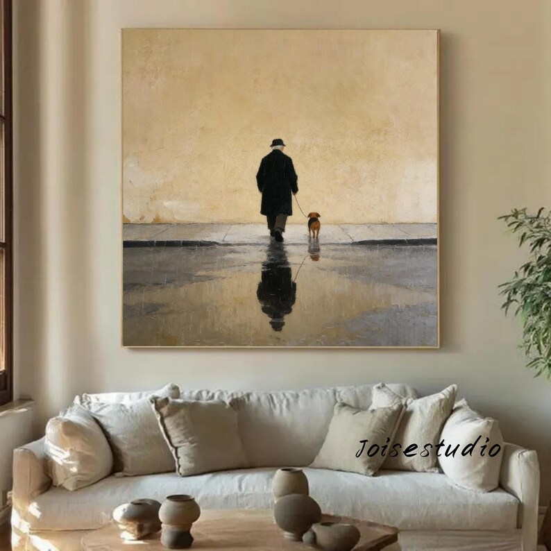 May include: An oil painting depicts a person in a black coat and hat walking a small brown dog on a wet street. The person's reflection is visible in the water. The background is a muted yellow, and the artwork is framed.