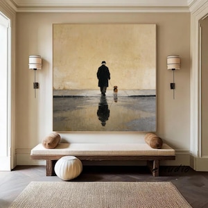 May include: Large framed artwork depicting a person walking a dog in the rain. The artwork features a muted color palette with a person in a black coat and hat, and a small brown dog. The person's reflection is visible in the water.