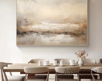May include: Abstract landscape painting in shades of brown, beige, and white. The painting depicts a horizon with a body of water in the foreground. The painting is framed in a gold frame and is hanging on a white wall above a wooden dining table.