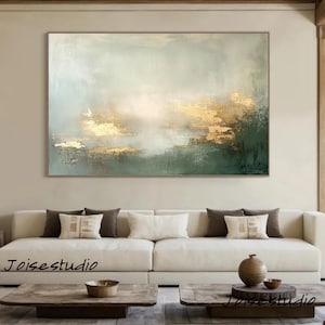 Puede incluir: Pintura abstracta de paisaje con una paleta de colores dorados, verdes y blancos. La obra de arte presenta pinceladas texturizadas y una forma rectangular. La pintura se exhibe sobre un sofá blanco en un salón.