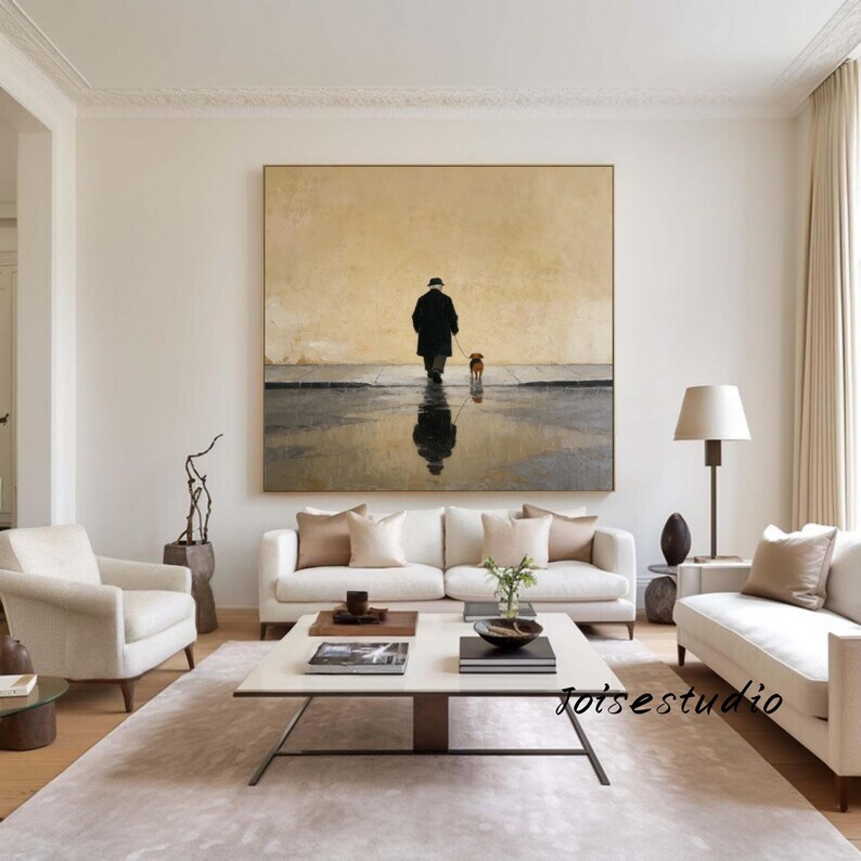 May include: A large framed painting depicts a person walking a dog on a wet surface, with the person's reflection visible. The artwork is in a neutral color palette, with a beige background and dark figures. The painting hangs above a white sofa.