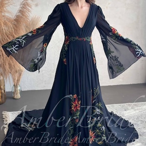 May include: A black, floor-length dress with long, sheer sleeves and a plunging neckline. The dress is adorned with colorful floral embroidery along the sleeves, waist, and skirt. The dress has a flowing silhouette and a train.