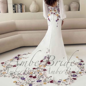 May include: White wedding dress with floral embroidery in red, purple, and yellow. The dress features long, sheer sleeves and a long train with matching floral detailing. The back of the dress has a row of buttons.