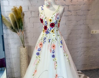 Puede incluir: Un vestido blanco de tul con escote en V y bordado floral. El bordado presenta una variedad de colores, incluyendo rosa, azul, amarillo y rojo.