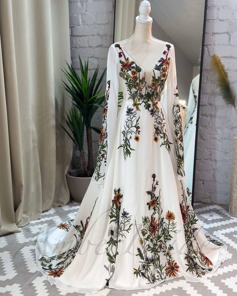 May include: A white maxi dress with long sleeves and a floral print. The dress has a V-neckline and a flowing skirt.
