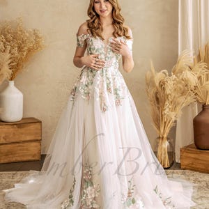 May include: A white off-the-shoulder wedding dress with floral embroidery. The dress has a fitted bodice and a flowing skirt.