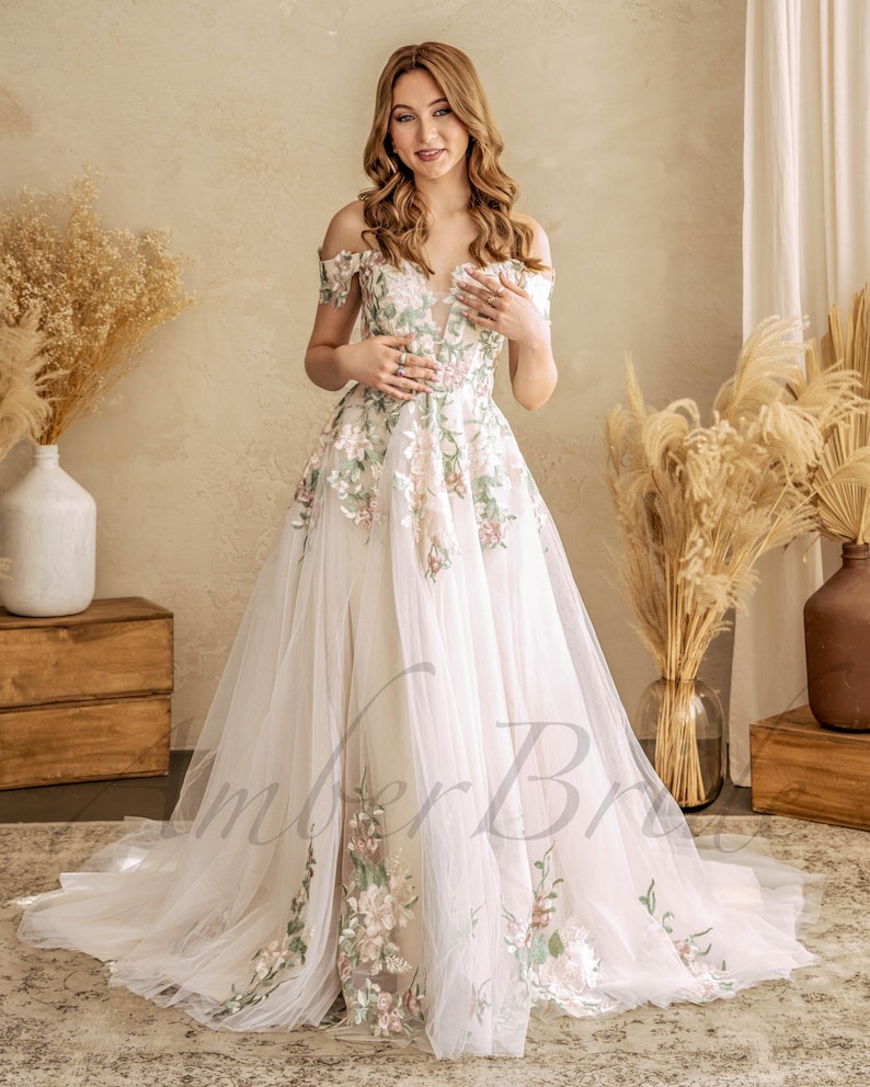 May include: A white off-the-shoulder wedding dress with floral embroidery. The dress has a fitted bodice and a flowing skirt.