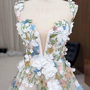May include: A white tulle dress with a plunging neckline and 3D floral embroidery in shades of white, blue, pink, and yellow.
