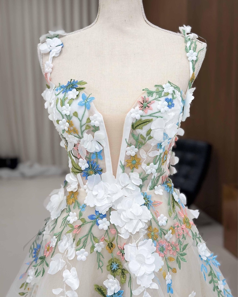 May include: A white tulle dress with a plunging neckline and 3D floral embroidery in shades of white, blue, pink, and yellow.
