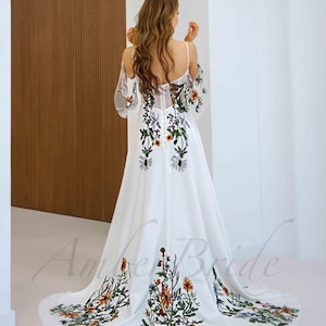 May include: White maxi dress with a floral embroidery design. The dress has a plunging neckline and a flowy skirt.
