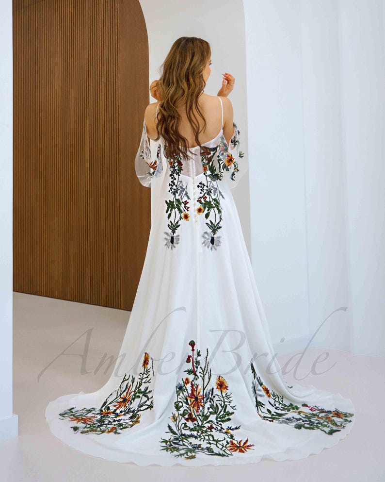 May include: White maxi dress with a floral embroidery design. The dress has a plunging neckline and a flowy skirt.
